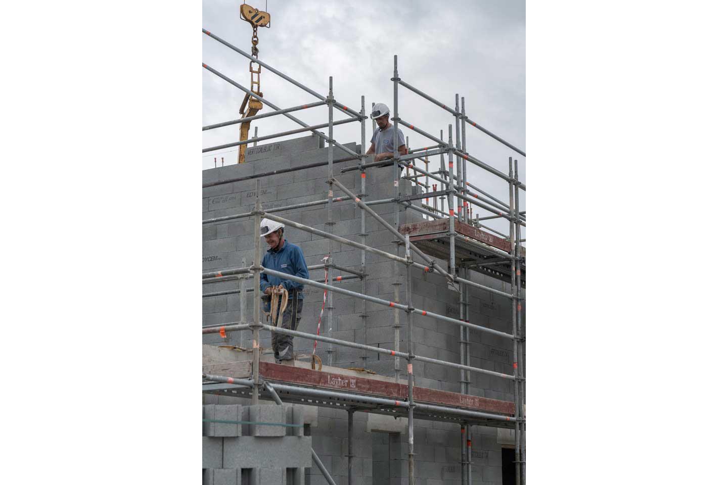 Deux ouvriers travaillent sur un échafaudage de construction d'une maison individuelle.