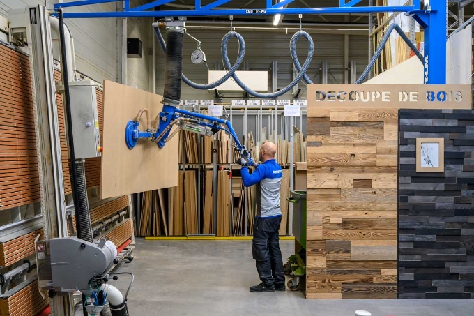 Un salarié utilise un préhenseur à ventouses dans l'atelier découpe de bois.