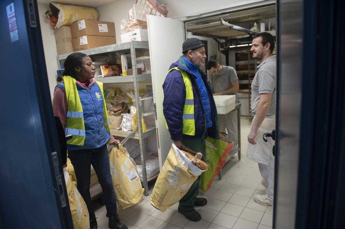 Éric et Marie chargent des sacs chez un boulanger lors de leur tournée d'enlèvement d'invendus. 