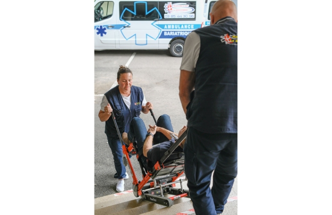 Deux ambulanciers réalisent le déplacement d'un patient à l'aide d'une chaise à chenilles avec assistance électrique.
