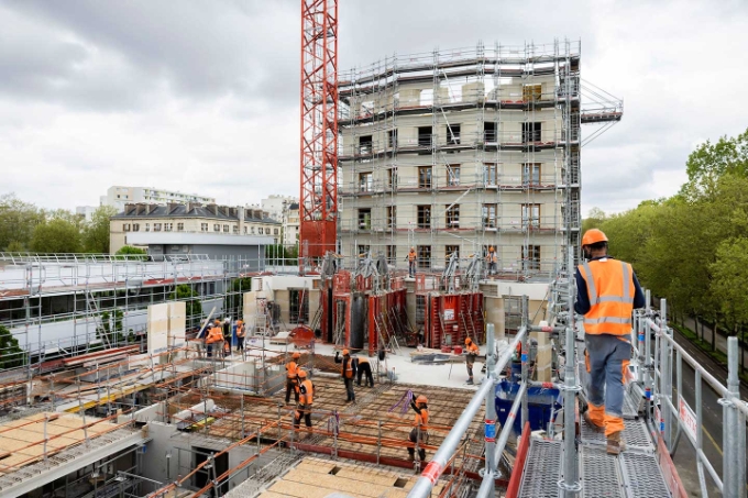 Les échafaudages couvrent l'étage en cours de construction. Des recettes à matériaux facilitent les approvisionnements à pied d'œuvre.