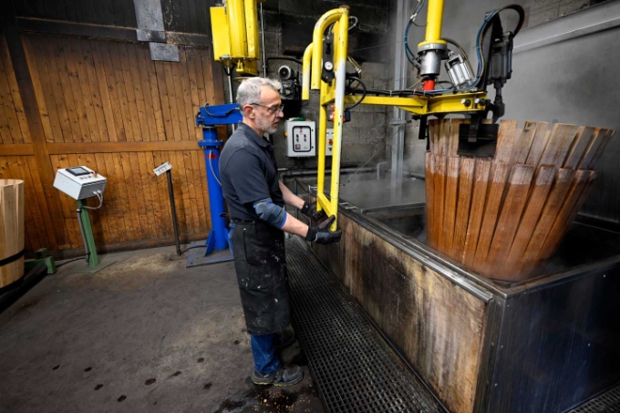 Le tonnelier déplace les tonneaux préformés à l'aide d'un bras manipulateur afin de les placer quelques minutes dans l'eau bouillante pour assouplir le bois.