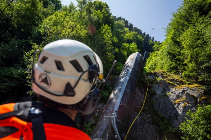 Sans jamais le quitter des yeux, le pilote mène son drone et la charge qu'il transporte au chantier en haut de la conduite forcée. Sans jamais le quitter des yeux, le pilote mène son drone et la charge qu'il transporte au chantier en haut de la conduite forcée.